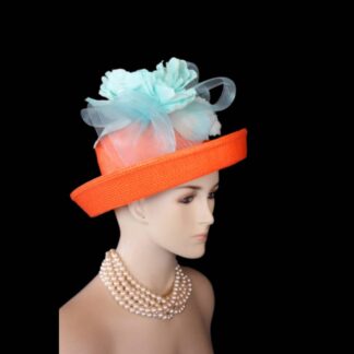 Introducing the epitome of luxury and refinement: the Ladies Orange Turquoise Aqua Formal Wedding Lift Up Brim Hat. This exquisite piece, crafted by the esteemed artisans at NYFashionHats.com, transcends mere headwear; it embodies a bold artistic vision that redefines elegance for the modern woman.