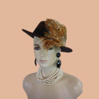Step into the realm of haute couture with the Ladies Dark Brown Gondola Bolero Gaucho Designer Hat—a true masterpiece that embodies the elegance and sophistication of high fashion. This striking boater-style hat, meticulously crafted by the renowned artisans at NYFashionHats.com, showcases an exquisite blend of sumptuous multi-colored brown, beige, gold and tan duck tiger feathers. Its daring design redefines what it means to make a fashion statement, ensuring that all eyes are on you at every occasion.
